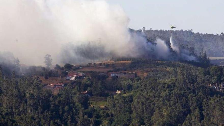 Un helicóptero intenta apagar las llamas del incendio de Negreira que amenazaba a varias casas. / ó. corral