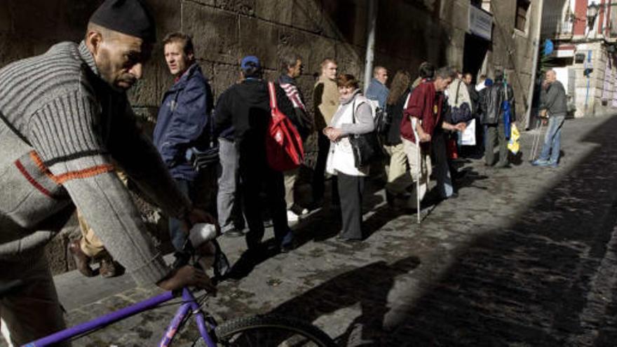 Un grupo de personas hace cola en la parte trasera de la concatedral de San Nicolás de Bari para que los voluntarios de Cáritas les entreguen un bocadillo.