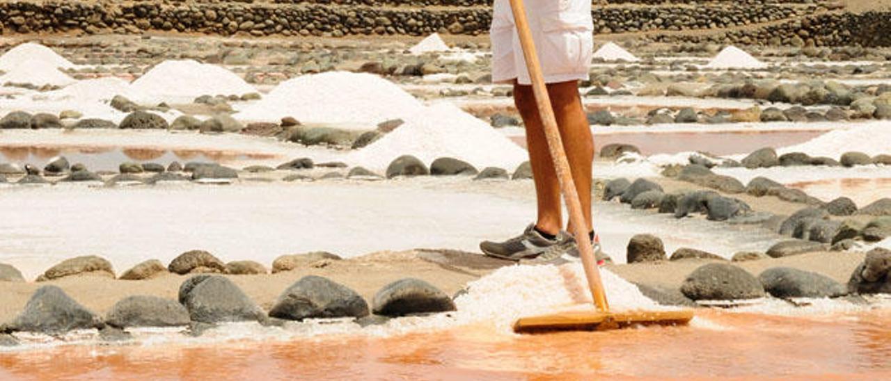 Josué Calderín, arrollando la sal hacia el balache, con unas aguas tintadas en naranja y rojo por las algas y crustáceos que cría la propia salmuera.