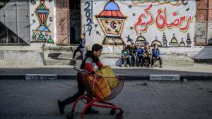 Un niño palestino empuja un carro con bidones de agua frente a un muro con dibujos temáticos del Ramadán en la ciudad de Gaza, este viernes.