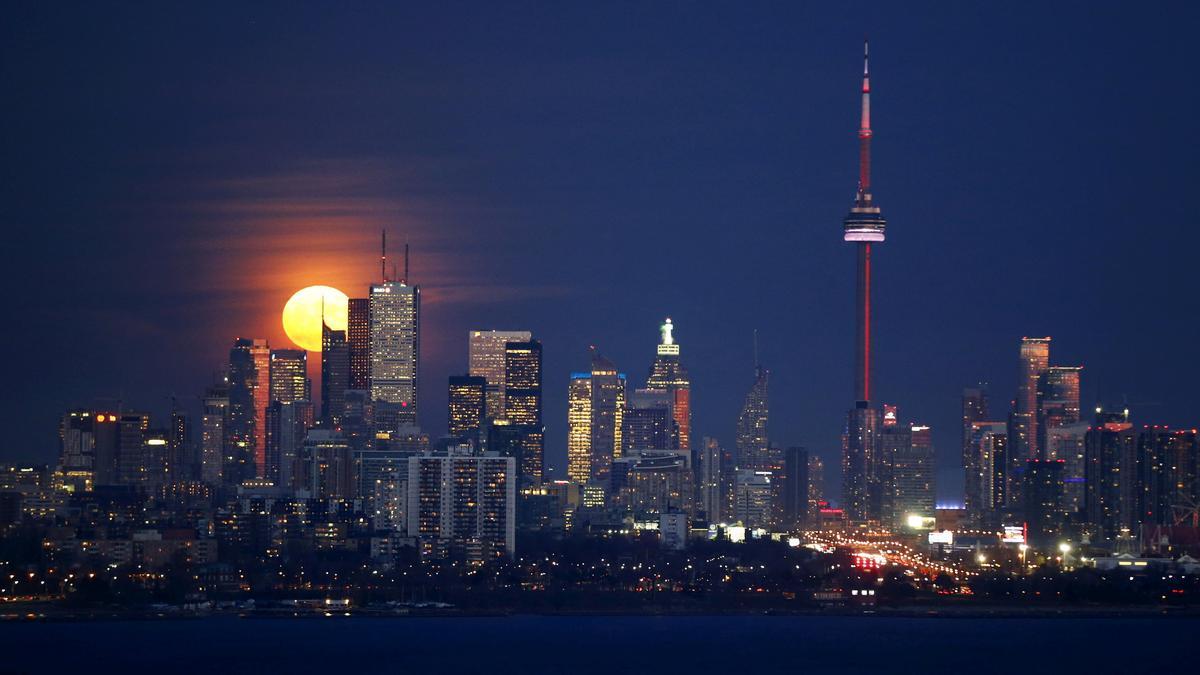 The moon rises behind the skyline and financial district in Toronto