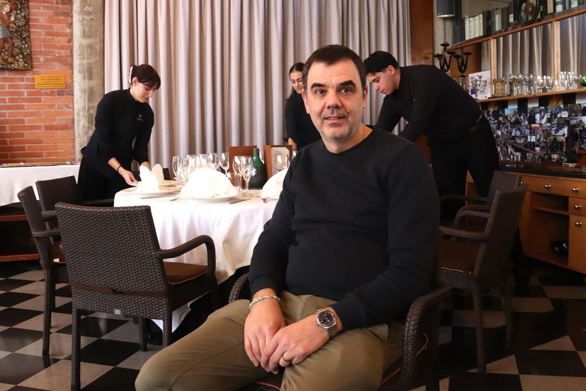 El director de l'Escola d'Hostaleria i Turisme de Girona, Jordi Garcia, assegut en una cadira mentre alguns alumnes fan pràctiques de sala