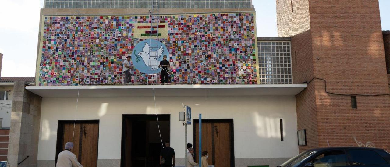 Un grupo de personas coloca el mural de ganchillo en la fachada principal de la iglesia de San José Obrero.