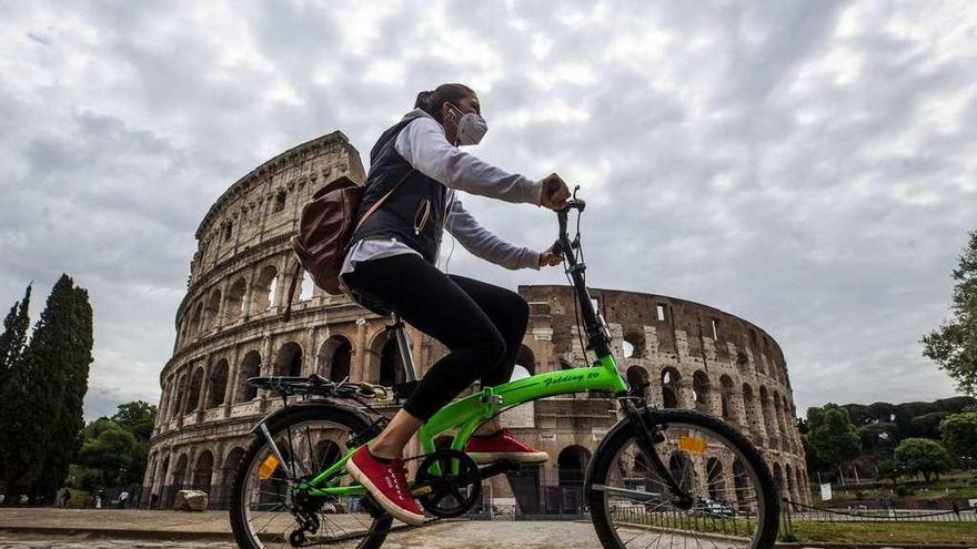 Una joven con mascarilla pasa en bicicleta junto al Coliseo en Roma.