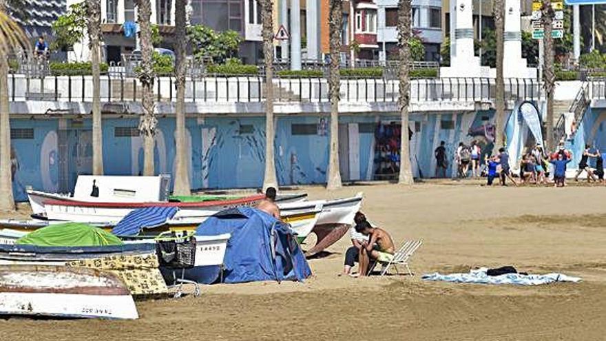 Tres personas sin techo el pasado sábado a las doce del mediodía en la playa de Las Alcaravaneras. Al lado, tres casetas, varias colchonetas y un carrito .