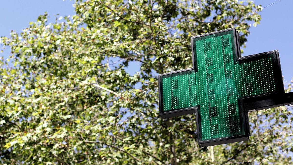 Una señal luminosa de la cruz verde a la entrada de una farmacia.