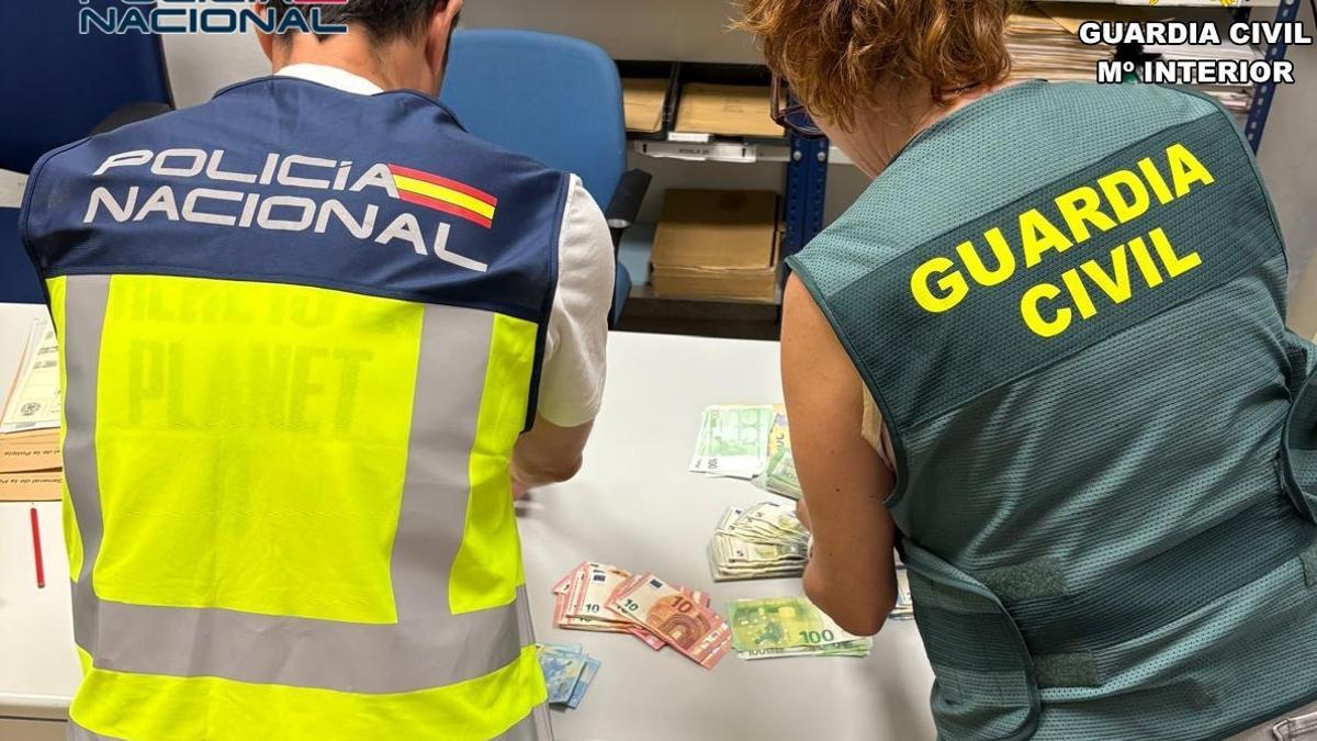 Un policía nacional y una guardia civil recuentan el dinero intervenido en los registros en Xàtiva y La Granja de la Costera.