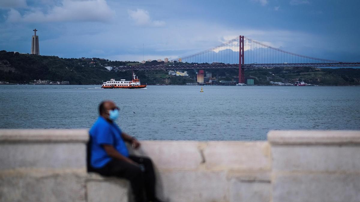 Un hombre con mascarilla sentado junto al río Tajo en Lisboa.