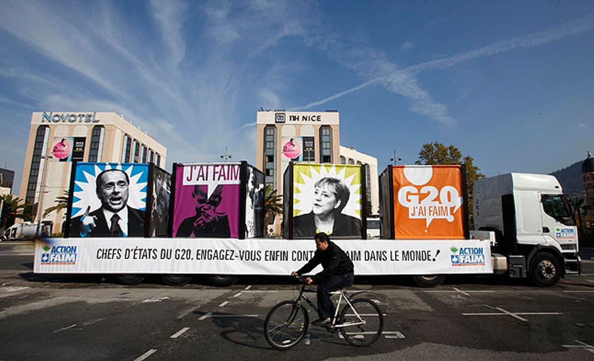 Un home passa en bicicleta davant d’un camió amb imatges de Silvio Berlusconi i Angela Merkel, al davant d’una manifestació contra el G-20  a Niça, l’1 de novembre.