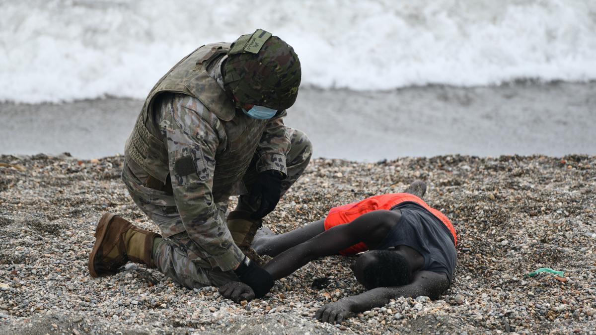 Un militar del ejército español ayuda a una persona tumbada en la orilla en una jornada marcada por las devoluciones en caliente que están efectuando a los migrantes que han entrado en Ceuta procedente de Marruecos