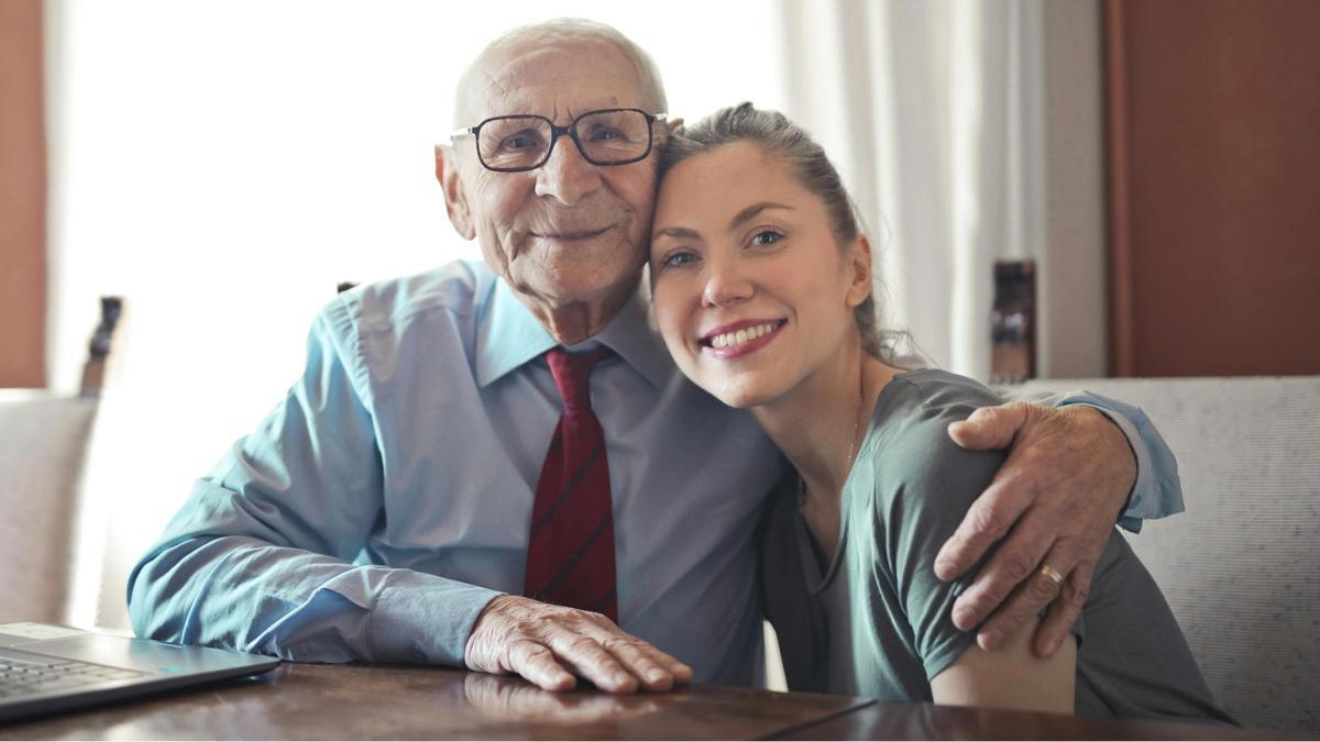 Un hombre mayor junto a una joven estudiante sentados en una mesa.