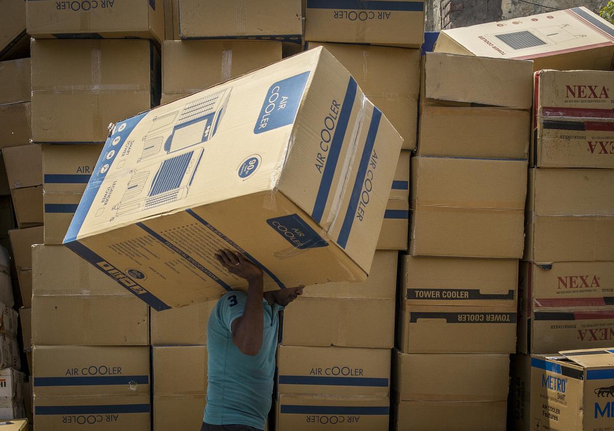 Un trabajador transporta un aparato de aire acondicionado, mientras pasa justo por delante de más cajas con otros aparatos para el mismo fin, almacenados para su venta en Nueva Delhi.
