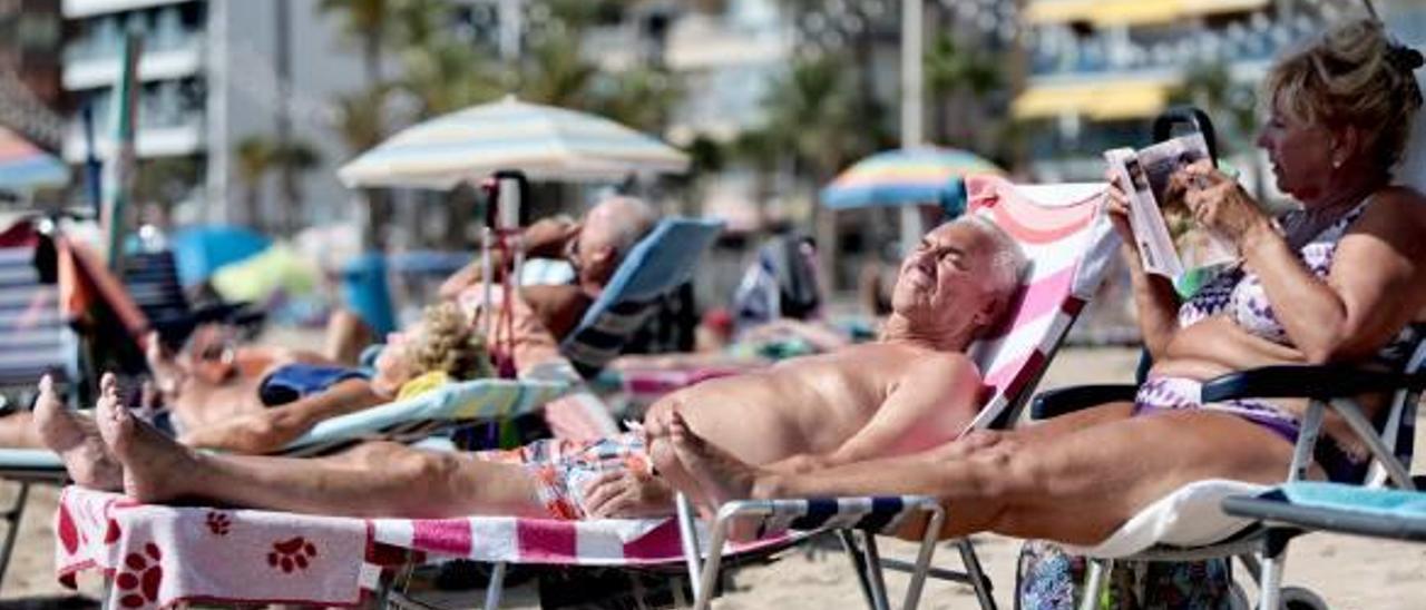 Un pareja de turistas jubilados toma el sol en la playa de Levante de Benidorm.