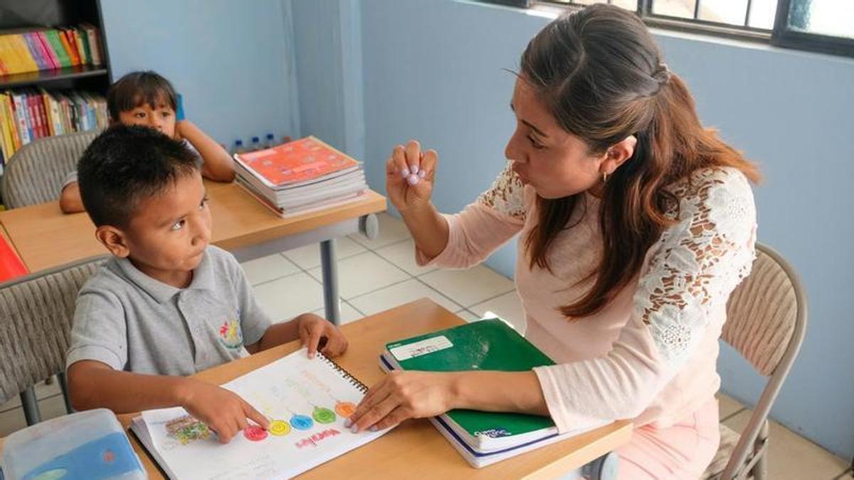 Una auxiliar ayuda a dos niños en un aula.