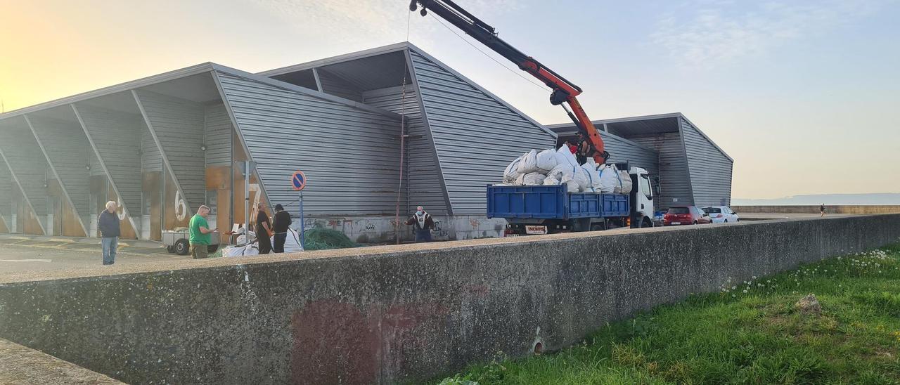 Un camión traslada los &quot;miños&quot; amontonados en el entorno de las casetas de usos pesqueros.