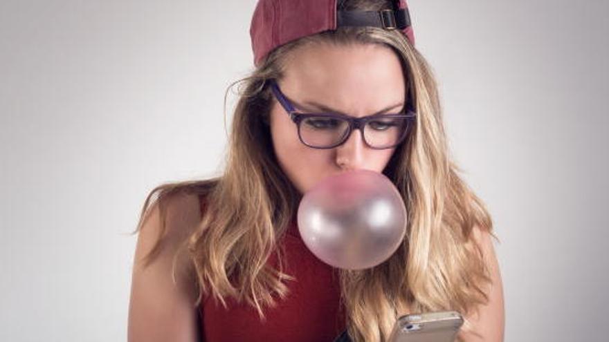 Una noia fent una bombolla amb el xiclet i mirant el seu mòbil