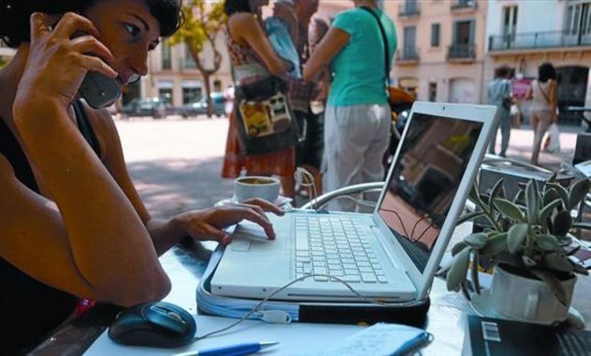 Una dona consulta internet en un portàtil mentre conversa pel mòbil, en una terrassa de Barcelona.
