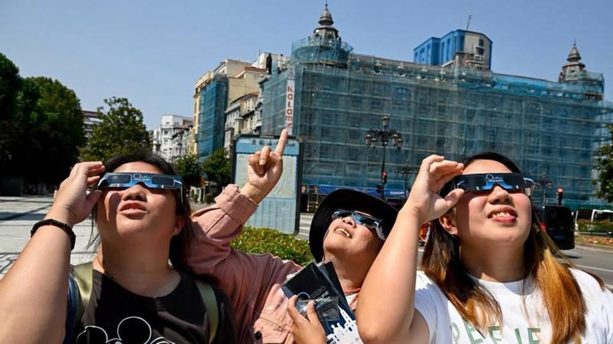 Tres turistas orientales probando las gafas del eclipse en el paseo de los Álamos.