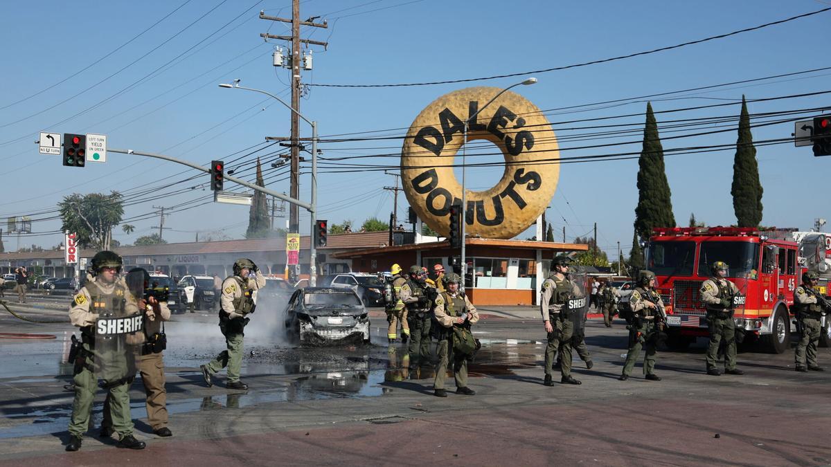 Las fuerzas del orden permanecen de pie frente a un coche quemado cerca de un Home Depot tras una redada llevada a cabo por el Servicio de Inmigración y Control de Aduanas (ICE) en Paramount, California,