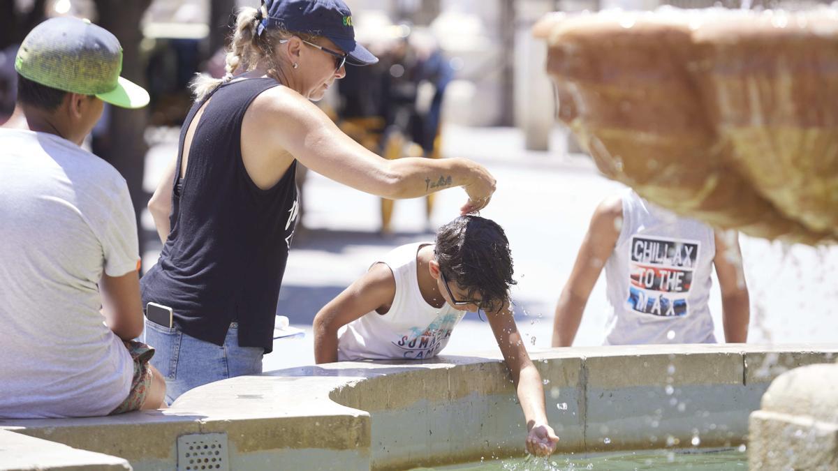 Varias personas se refrescan en una fuente en plena ola de calor, este verano.