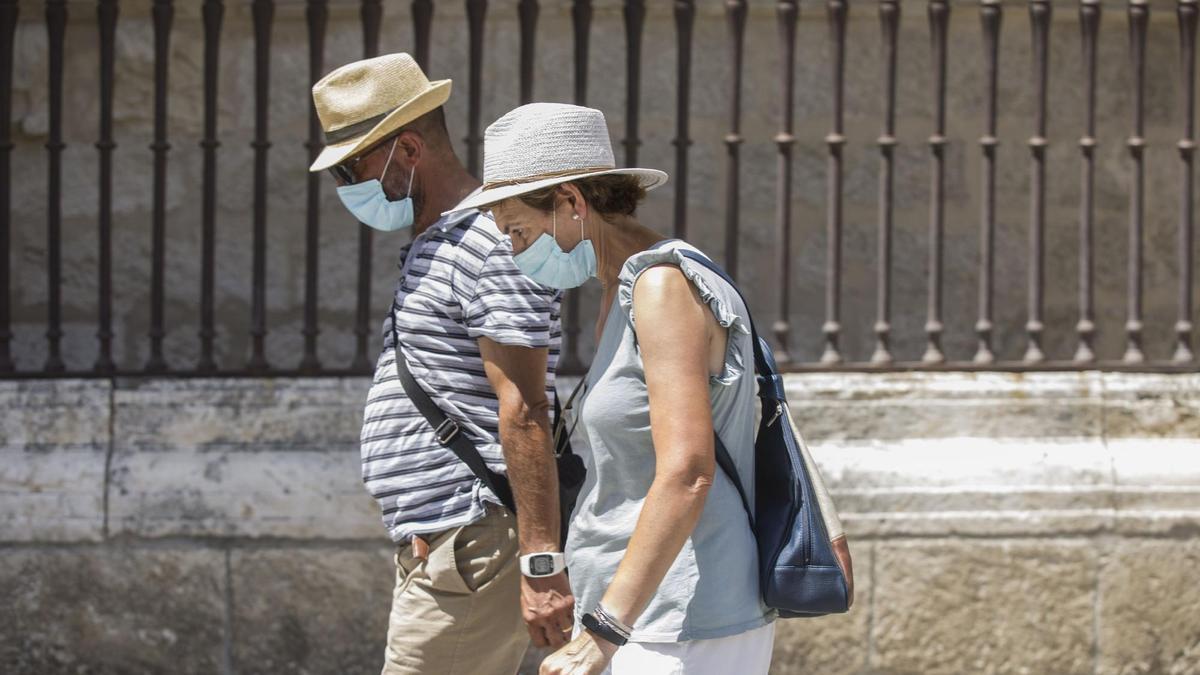 Dos personas caminan con mascarilla y sombrero durante la ola de calor.