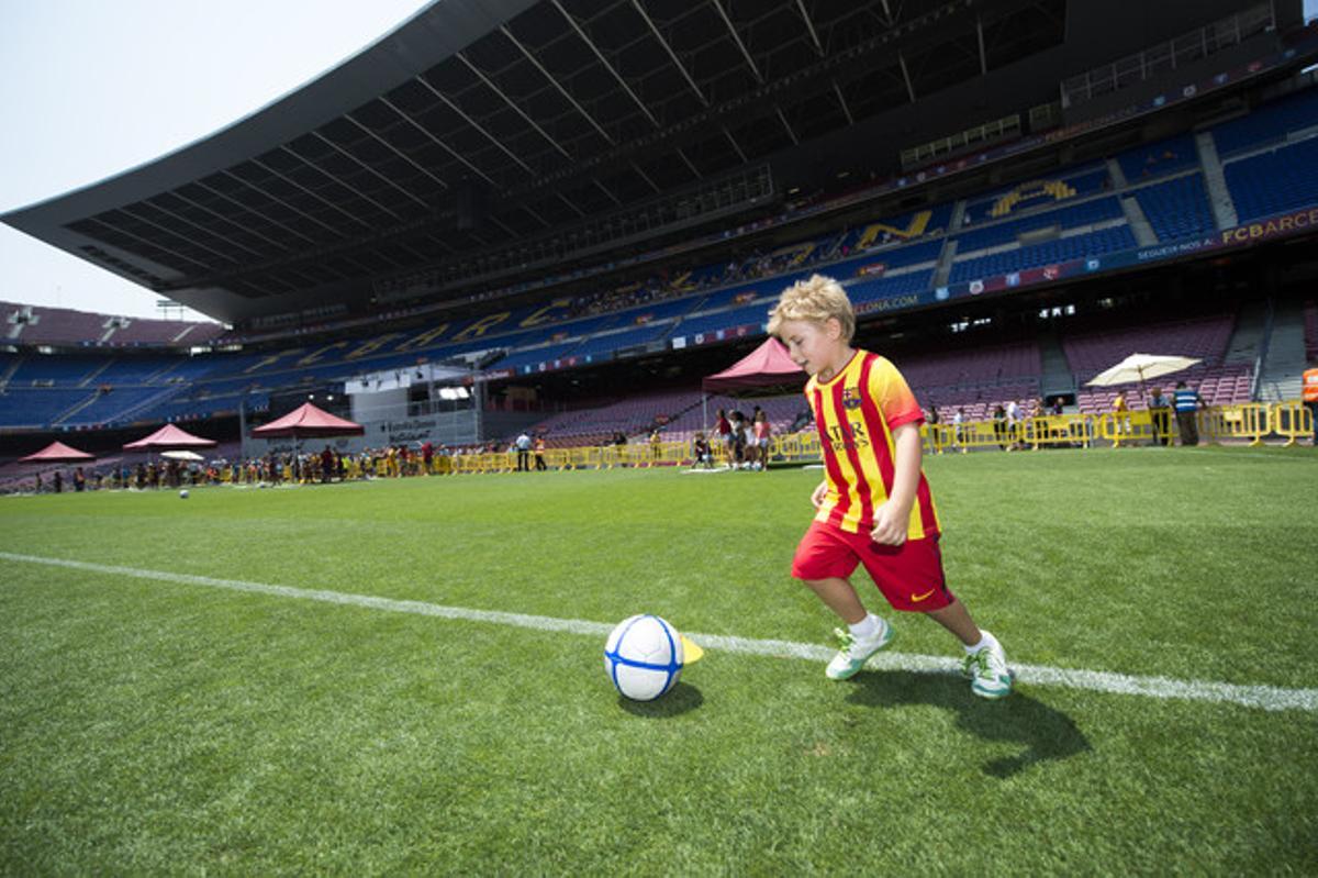 Un jove seguidor culer corre amb la pilota per la gespa del Camp Nou.