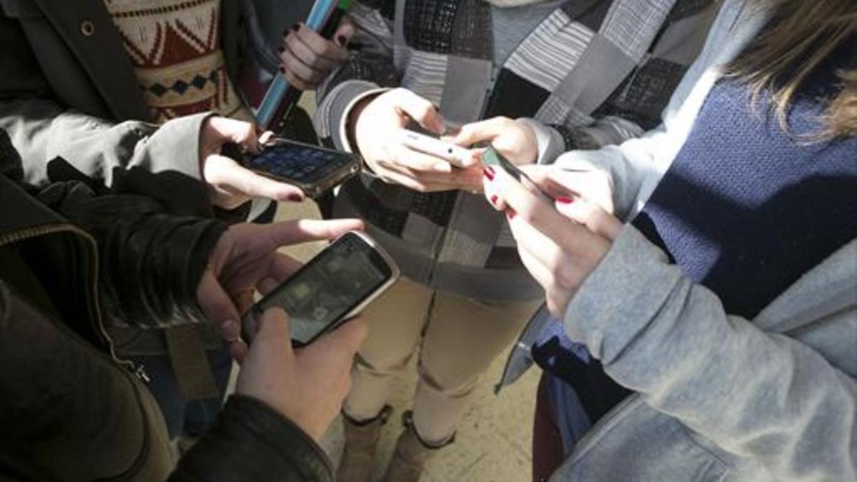 Cuatro jóvenes manipulan sus móviles.