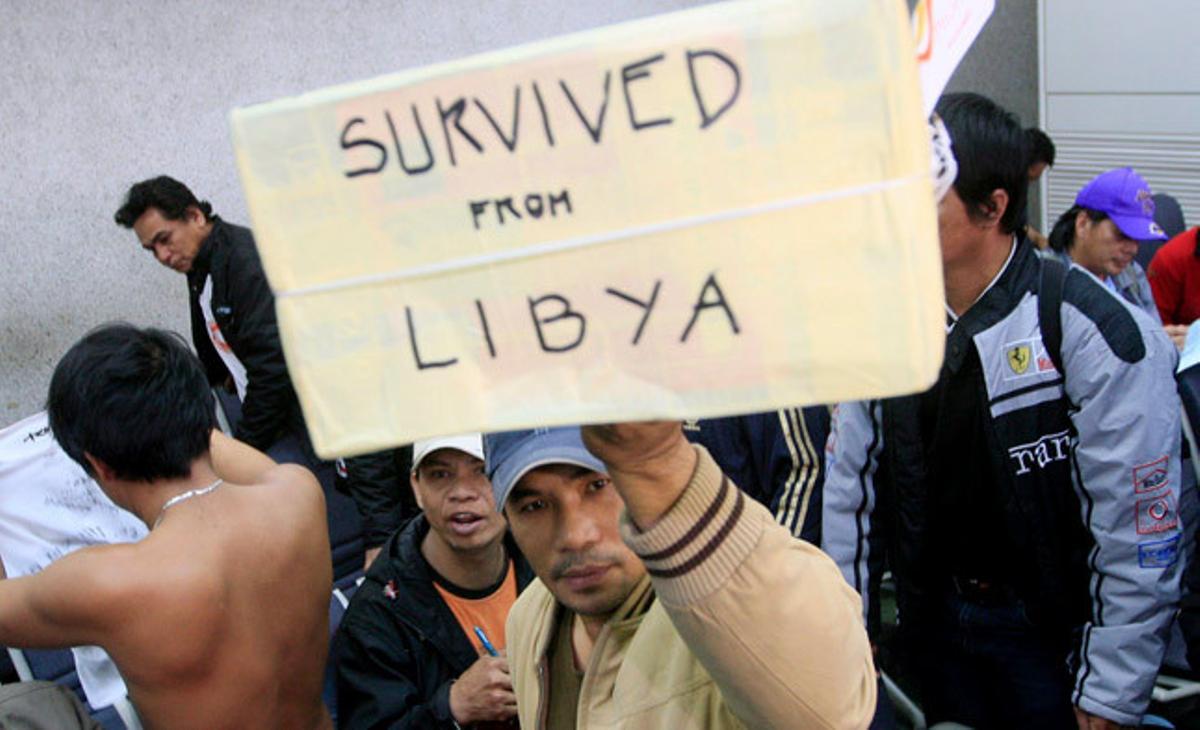 Un treballador filipí acabat d’arribar a Manila des de Líbia porta una caixa amb la inscripció Va sobreviure a Líbia. Un treballador filipí acabat d’arribar a Manila des de Líbia porta una caixa amb la inscripció Va sobreviure a Líbia.