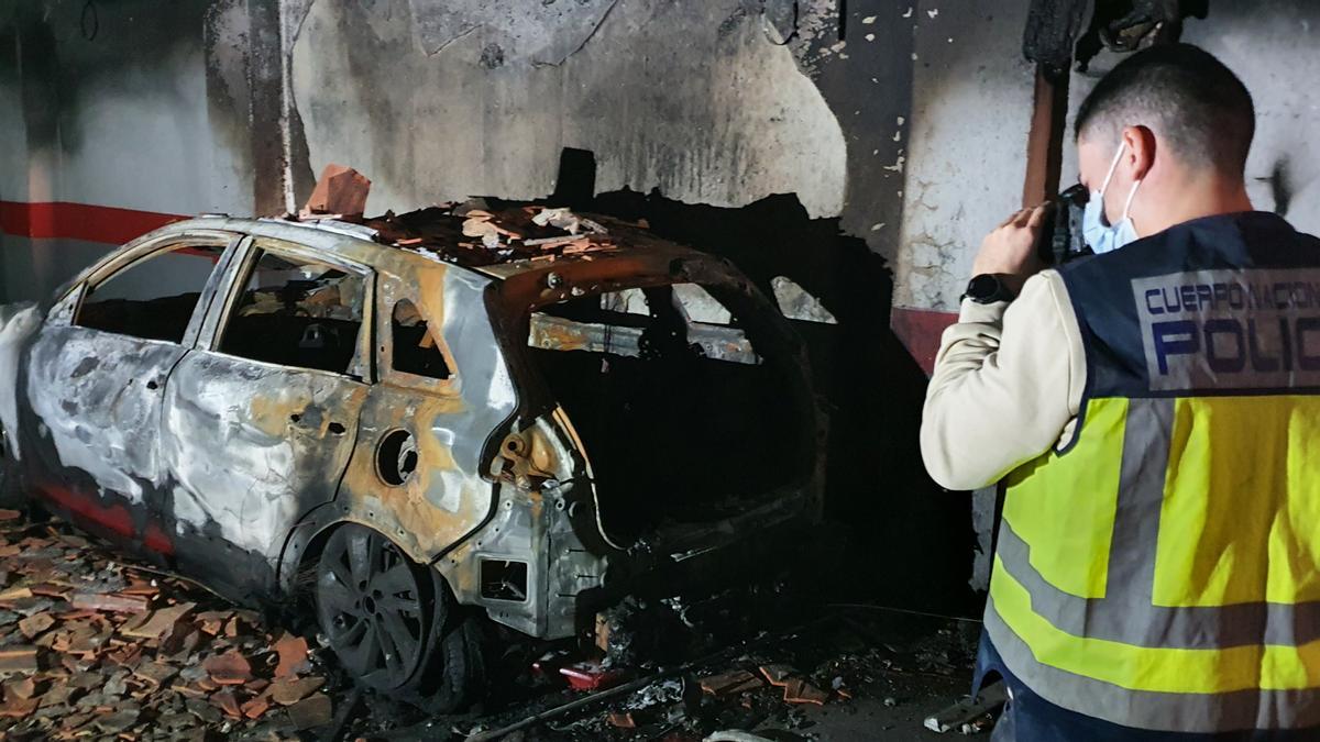 Un agente de la Policía Científica inspeccionando el vehículo incendiado en un garaje de Alicante.