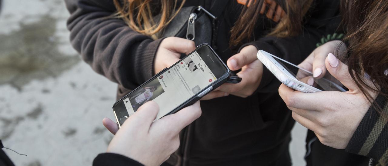 Tres jóvenes consultan sus teléfonos inteligentes.