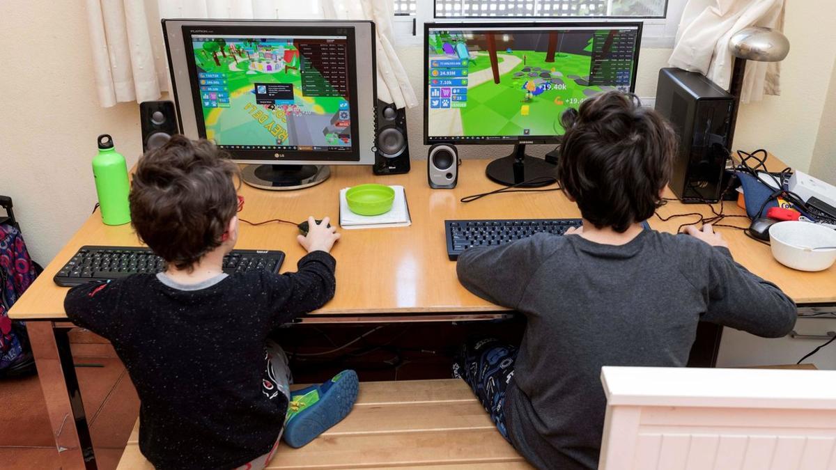 Dos niños juegan en sus ordenadores durante el confinamiento, en Murcia, el 28 de marzo