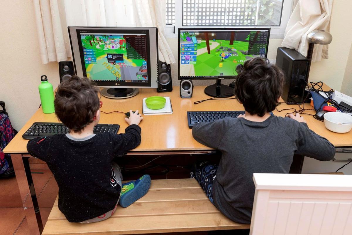 Dos niños juegan en sus ordenadores durante el confinamiento, en Murcia, el 28 de marzo.