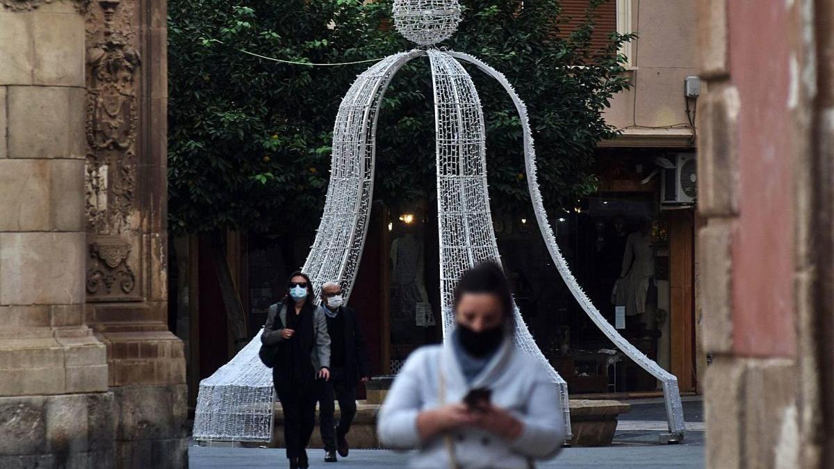 Personas con mascarilla pasan junto a un adorno navideño instalado en Murcia.