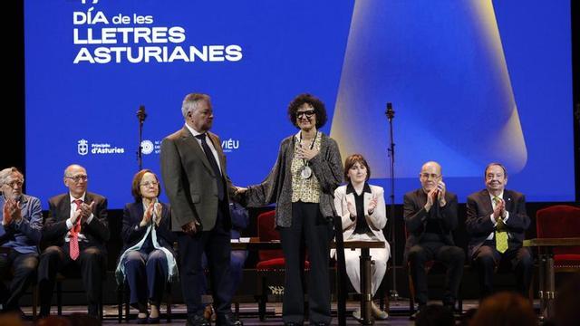 Berta Piñán, tras recibir el Premiu Nacional de Lliteratura Asturiana de manos de Xosé Antón González Riaño, a su lado, sobre el escenario del Campoamor y ante los miembros de la Academia de la Llingua, sentados tras ellos.  | LUISMA MURIAS