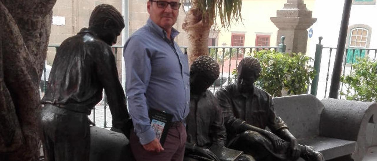 Faneque Hernández, con su nuevo libro en la mano, junto a una escultura grupal en la plaza del Rosario, en Agüimes.