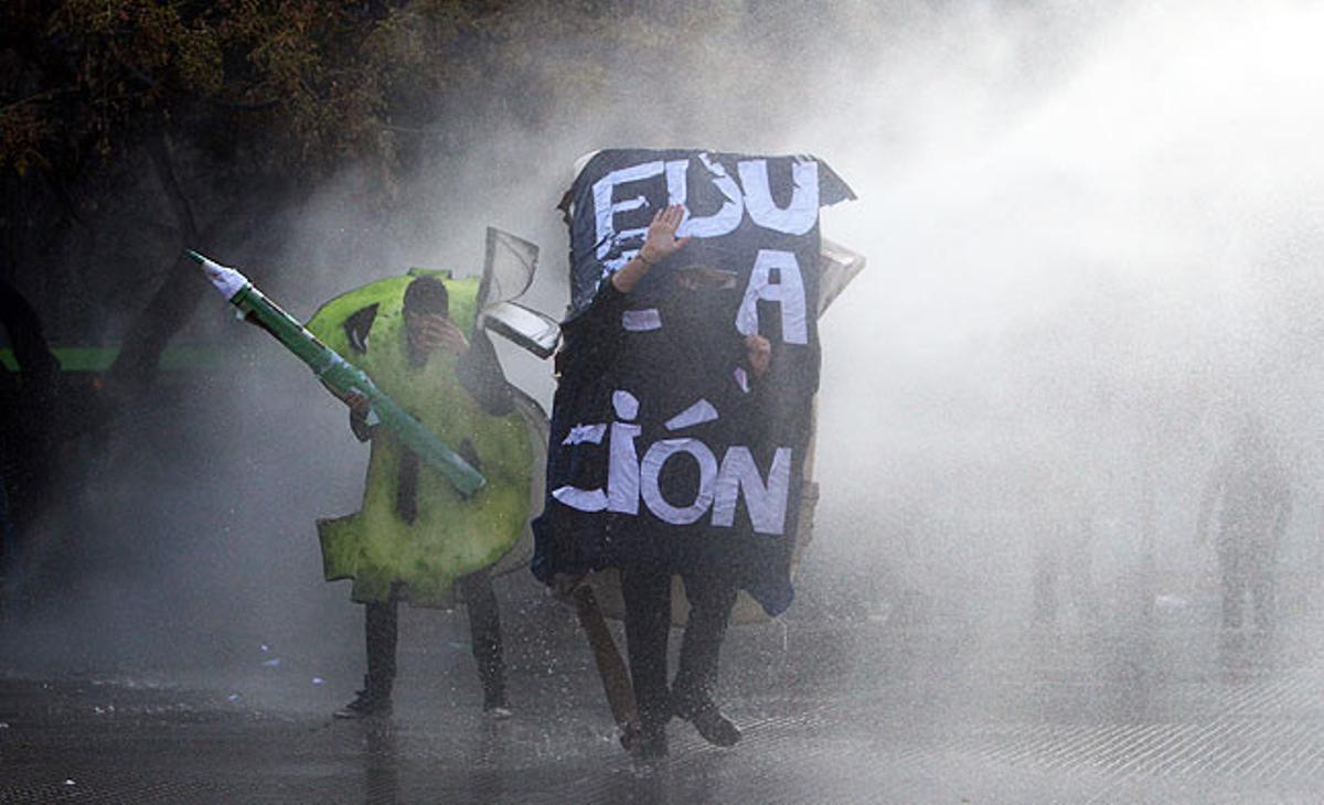 Uns estudiants xilens disfressats s’enfronten a la policia aquest dijous a la ciutat de Santiago. Més de 70.000 persones han participat en una multitudinària manifestació per exigir reformes en l’educació pública.