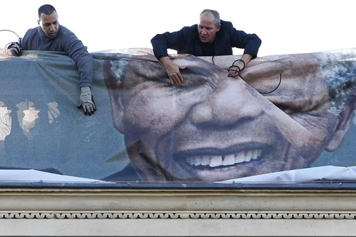 Dos homes despleguen, divendres, un mural amb la cara de Mandela que cobreix la façana del Ministeri d’Afers Estrangers francès, a París.