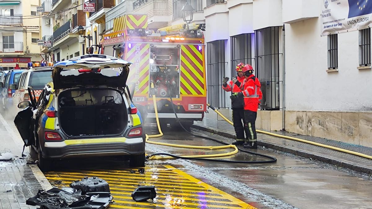 Bomberos extinguen el fuego producido en un coche de la Policía Local de Palma del Río.