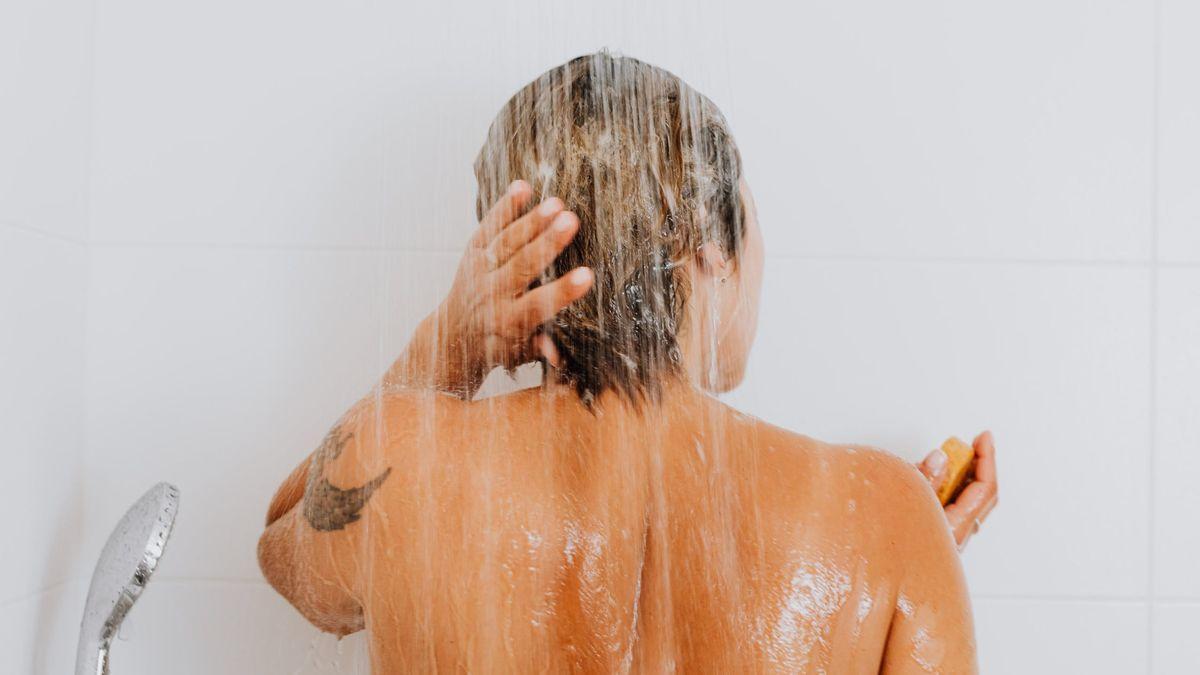 Una mujer se lava el pelo en la ducha.