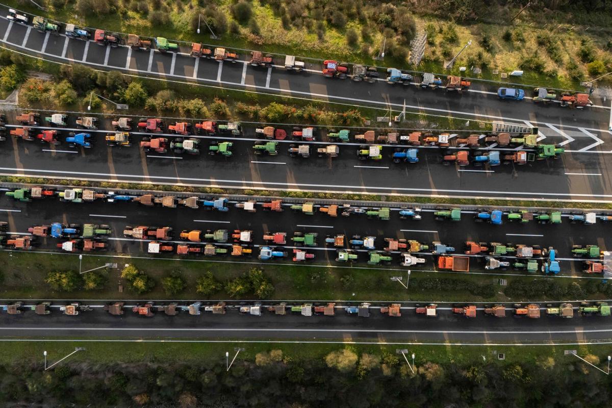 TOPSHOT - An aerial view shows tractors of farmers blocking the national highway outside the central Greek city of Karditsa on December 8, 2025 to demand swifter access to EU subsidies. Greek farmers demanding the payment of EU subsidies on December 8 shut down the two main international airports on the island of Crete after clashing with riot police in a growing showdown with the government. (Photo by Aris MESSINIS / AFP)