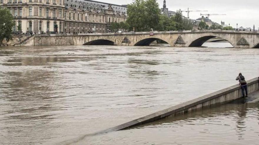 Varias personas observan el nivel del Sena a su paso por el Pont Royal de París.