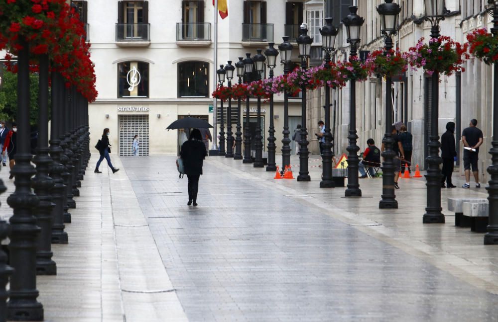 Imágenes de una lluviosa mañana de jueves en el centro de Málaga, donde al paisaje ya habitual de pocas personas y la mayoría de ellas con guantes y mascarillas se le han añadido los preparativos de bares, cafeterías y terrazas que se preparan para el inminente cambio de fase de la desescalada de la ciudad.