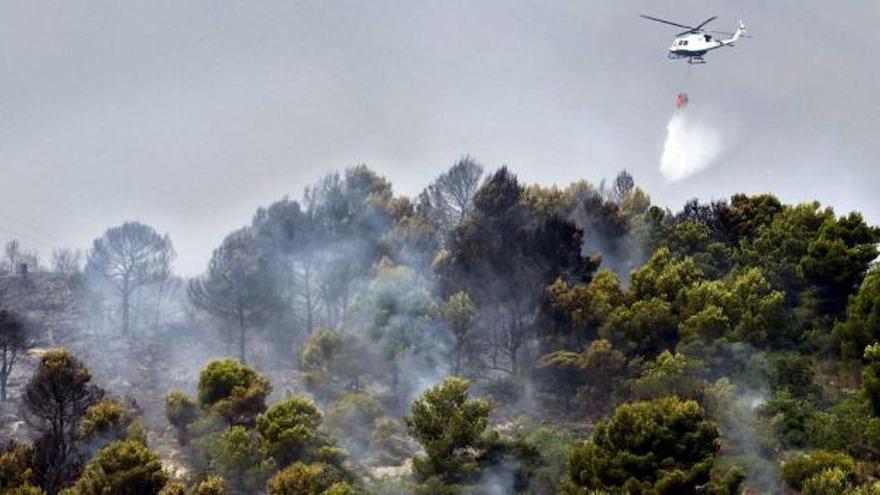Un helicóptero arroja agua sobre una zona boscosa que está ardiendo.