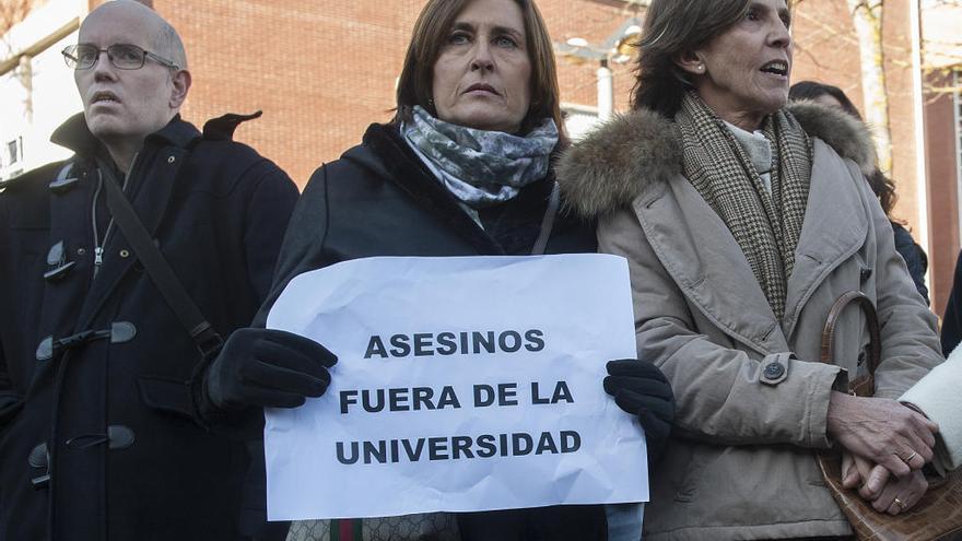 Una mujer sostiene un cartel en el que se lee &quot;Asesinos fuera de la Universidad&quot;.