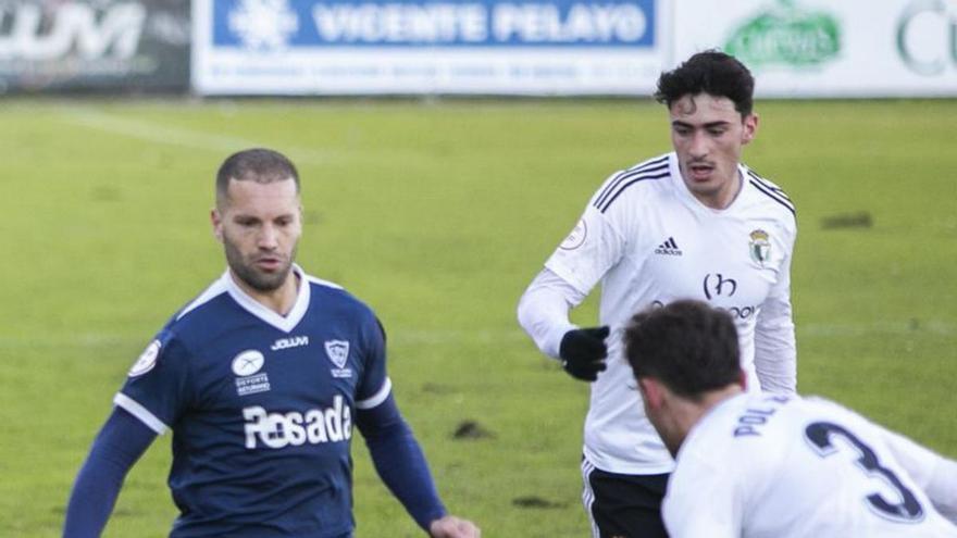 Lora, con el balón, ante dos jugadores del Burgos Promesas durante el partido de ayer. | María Fuentes