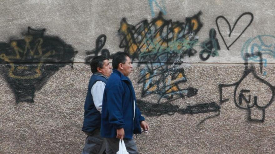 Dos viandantes pasan junto a unas pintadas de bandas latinas, las coronas de tres puntas son uno de sus símbolos.