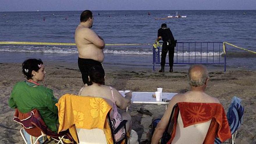 Un policía acordona la playa de la Albufereta ante la mirada de cuatro bañistas.