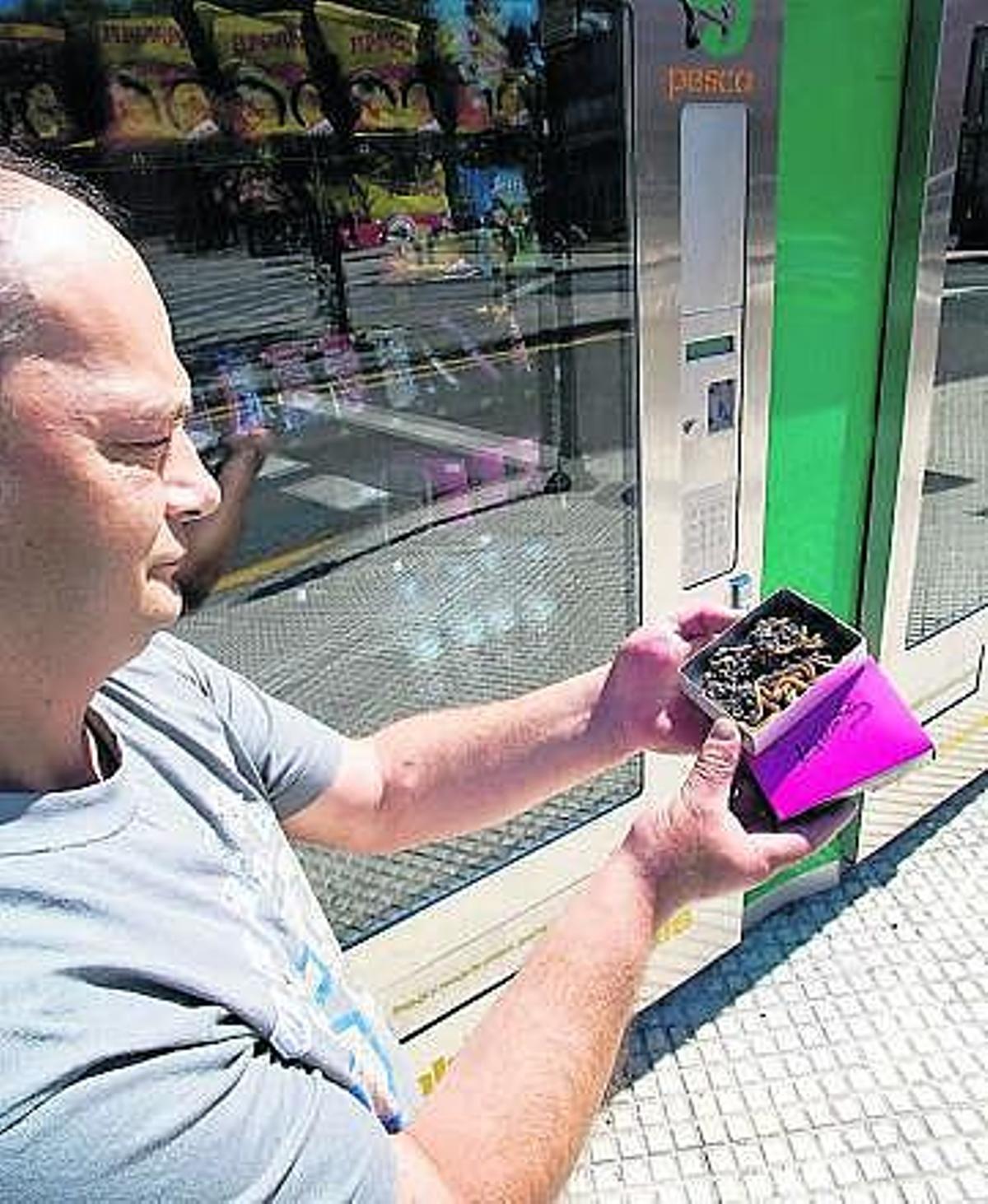 José Luis González muestra una caja con cebo junto a la expendedora.
