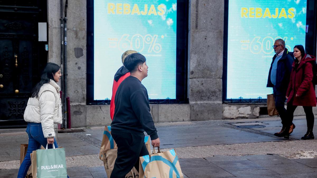 Varias personas caminan por una calle comercial de Madrid tras comprar en las rebajas