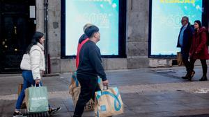 Varias personas caminan por una calle comercial de Madrid tras comprar en las rebajas